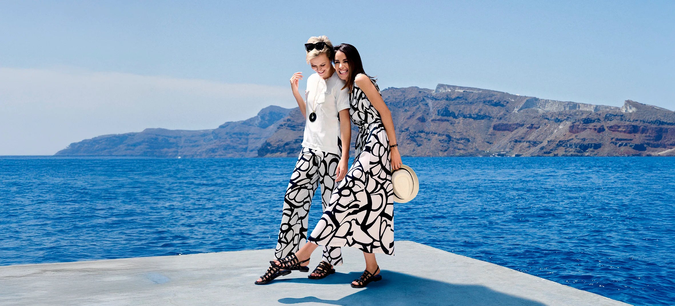 2 modelshaving fun in front of the sea in Greece. Wearing black and white outfits